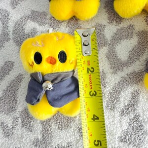 May include: A plush yellow chick with black eyes, an orange beak, and a grey vest. The chick is approximately 5 cm tall, as measured by a yellow and silver Stanley tape measure.