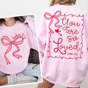 May include: Pink sweatshirt with a pink bow and the text "John 3:16" on the front. The back of the sweatshirt has a pink bow and the text "You are so Loved John 3:16" inside a red frame.