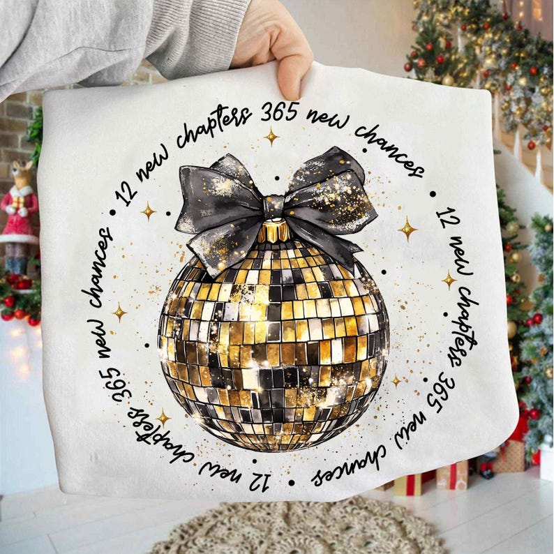 Pu&ograve; includere: Un cuscino bianco con un design a palla da discoteca oro e nero e un fiocco nero. Il cuscino ha il testo "12 nuovi capitoli 365 nuove possibilit&agrave;" in un motivo circolare attorno alla palla da discoteca. Il cuscino &egrave; tenuto da una persona.
