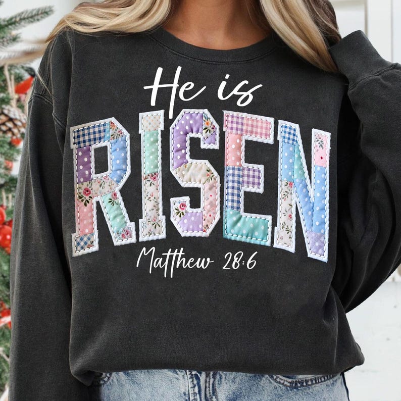 Puede incluir: Sudadera gris oscuro con las palabras "He is RISEN" en un dise&ntilde;o de patchwork. La palabra "RISEN" est&aacute; hecha de varias telas de colores pastel. El texto "Matthew 28:6" est&aacute; escrito debajo.