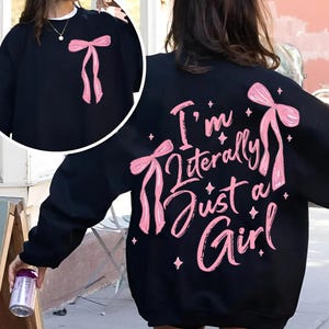 May include: Black sweatshirt with pink bows and the text "I'm literally just a girl" printed on the back.
