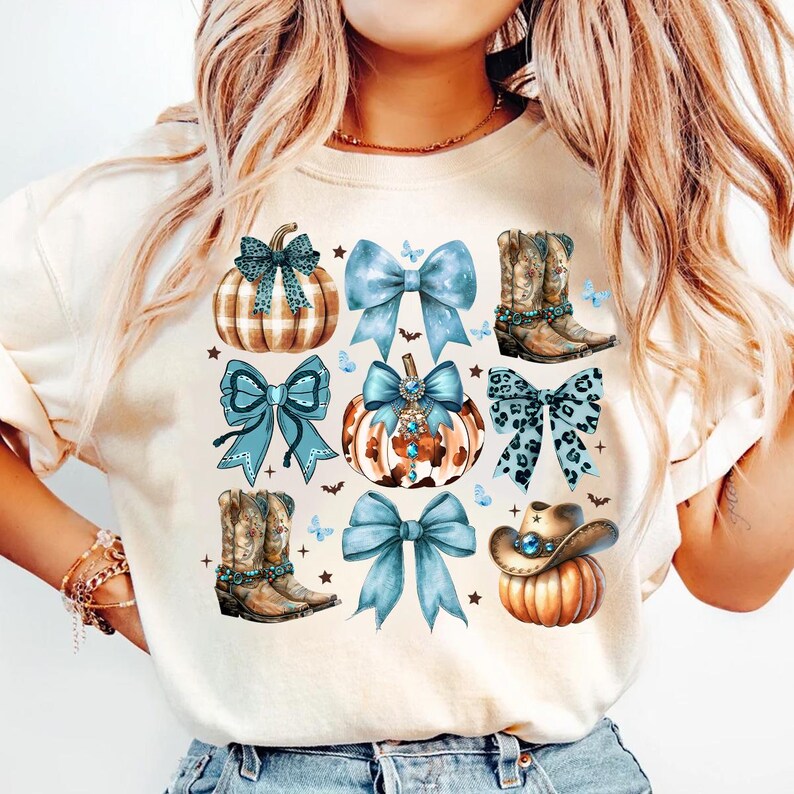 May include: A white t-shirt with a blue, brown, and white design featuring pumpkins, bows, cowboy boots, and butterflies.