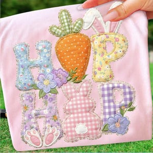 Pode incluir: Tecido rosa com a palavra "HOP" escrita em letras de patchwork coloridas. O "H" é floral azul, o "O" é uma cenoura laranja e o "P" é floral amarelo. Um coelho rosa e flores roxas também são apresentados.