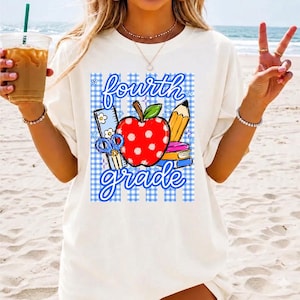 K&ouml;nnte beinhalten: Cremefarbenes T-Shirt mit einem Design f&uuml;r die vierte Klasse. Das Design zeigt einen roten Apfel mit wei&szlig;en Punkten, einen Bleistift, B&uuml;cher, eine Schere und die Worte "fourth grade" in einer verspielten Schriftart, vor blauem Vichy-Hintergrund.