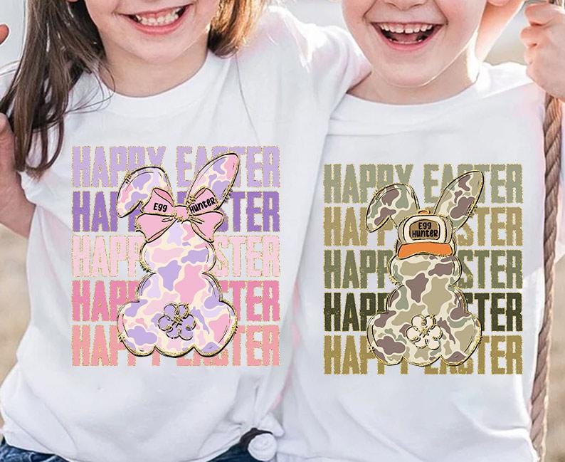 May include: Two white t-shirts with a graphic of a bunny rabbit. The bunny on the left is pink and purple with a bow and the text "Egg Hunter". The bunny on the right is camouflage with a hat and the text "Egg Hunter". Both shirts have the text "Happy Easter" repeated multiple times.