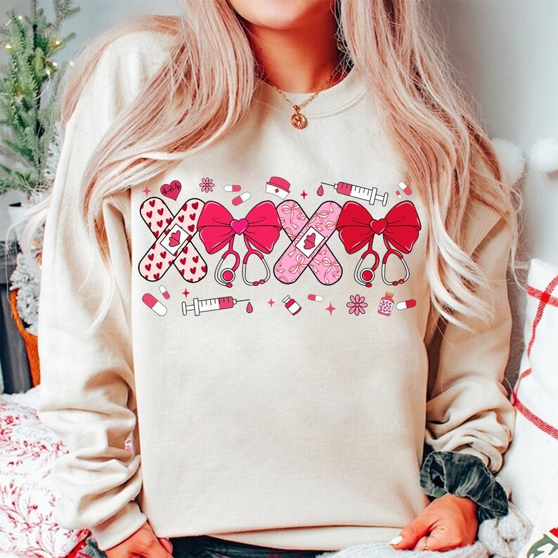 May include: A cream-colored sweatshirt with a pink and red design featuring band-aids, hearts, bows, stethoscopes, and syringes.