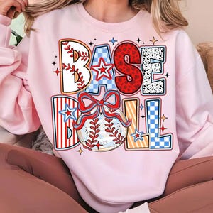 May include: A pink sweatshirt with a colorful graphic design that says "BASEBALL" with a baseball and a bow.