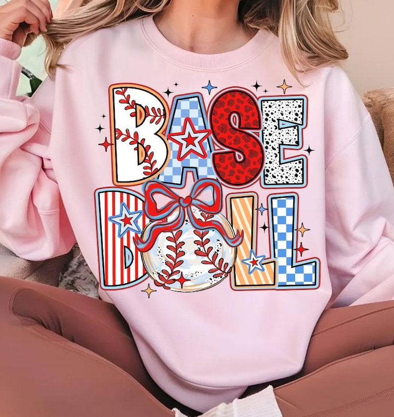 May include: A pink sweatshirt with a colorful graphic design that says "BASEBALL" with a baseball and a bow.