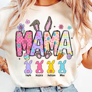 May include: A white t-shirt with a colorful "MAMA" design featuring bunny ears, Easter eggs, and flowers. Below the design are four bunny silhouettes with the names Layla, Jessica, Jackson, and Max.