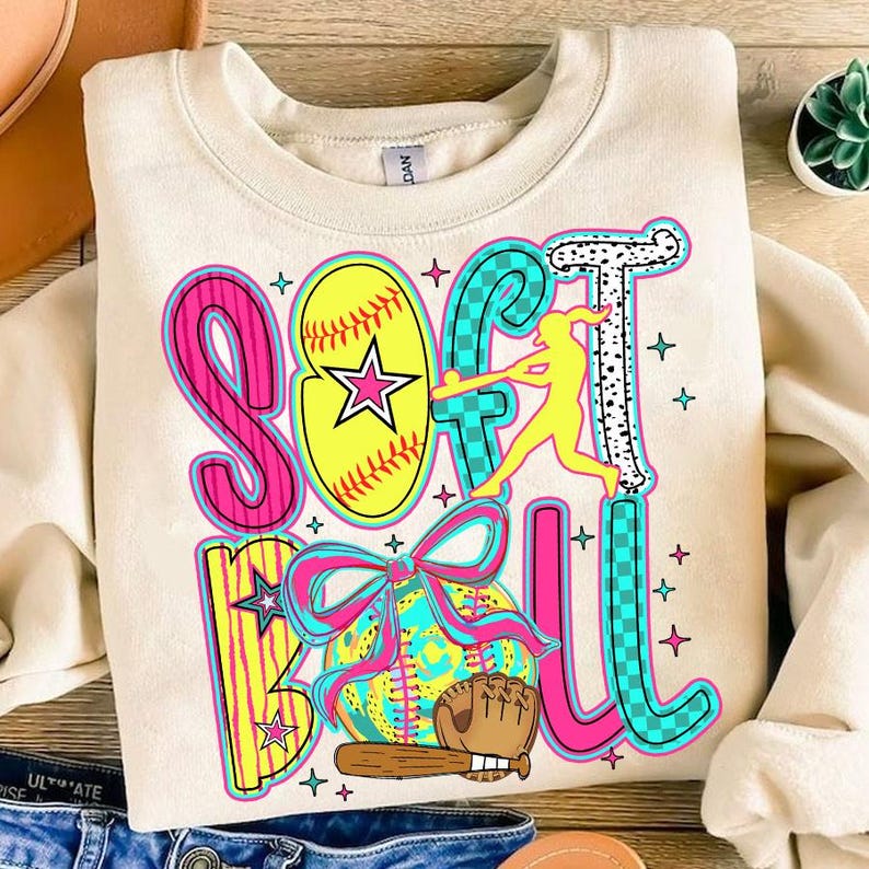 May include: A cream-colored sweatshirt with a colorful graphic design that says "Softball" with a softball, a bat, a glove, and a player in a softball pose.