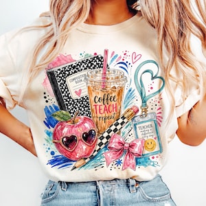 Puede incluir: Una camiseta color crema con un estampado gráfico de un cuaderno, un vaso de café helado con el texto coffee TEACH repeat, una manzana roja con gafas de corazón, un lápiz, un lazo rosa y una tarjeta de identificación de profesor con una cara sonriente.