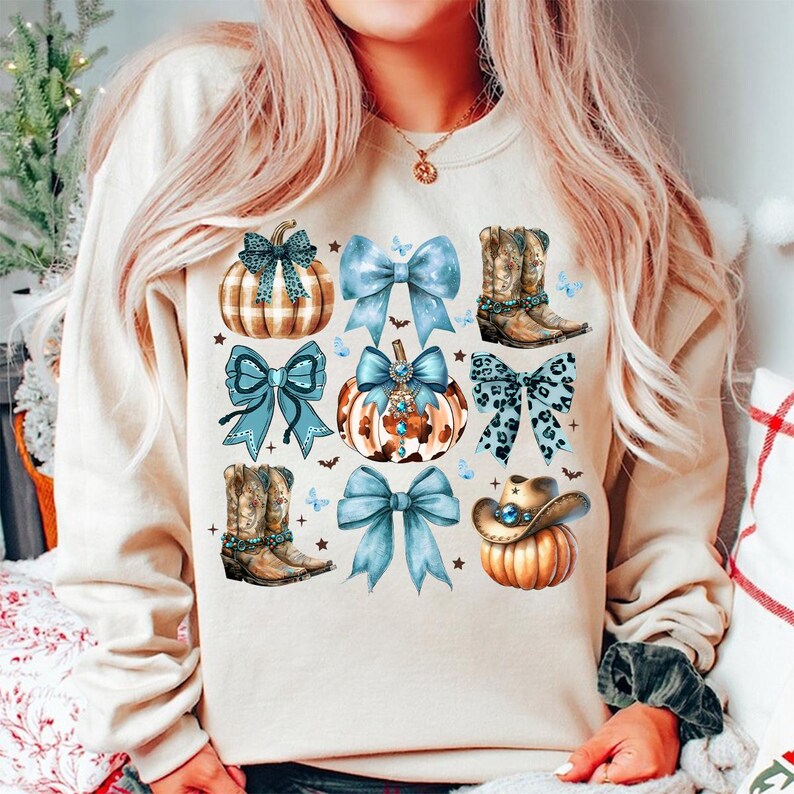 May include: A cream-colored sweatshirt with a fall-themed design featuring pumpkins, bows, and cowboy boots. The pumpkins are decorated with plaid, leopard print, and rhinestones. The bows are blue with white polka dots. The cowboy boots are brown with blue embellishments.