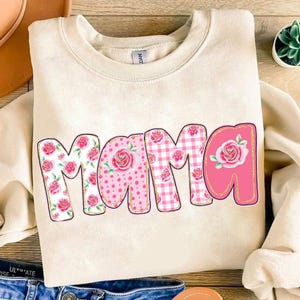 May include: A cream colored sweatshirt with the word "Mama" in pink letters. The letters are decorated with a patchwork design of pink flowers, polka dots, and gingham.