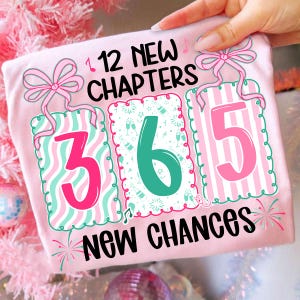 May include: A light pink t-shirt with the text "12 NEW CHAPTERS 365 NEW CHANCES". The numbers 3, 6, and 5 are in decorative frames with pink and teal accents. Pink bows and musical notes are also featured.