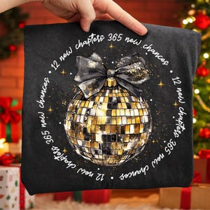 Pu&ograve; includere: Cuscino decorativo nero con un design a palla da discoteca oro e nero e un fiocco nero. Il cuscino ha il testo "12 nuovi capitoli 365 nuove possibilit&agrave;" in un motivo circolare attorno alla palla da discoteca.