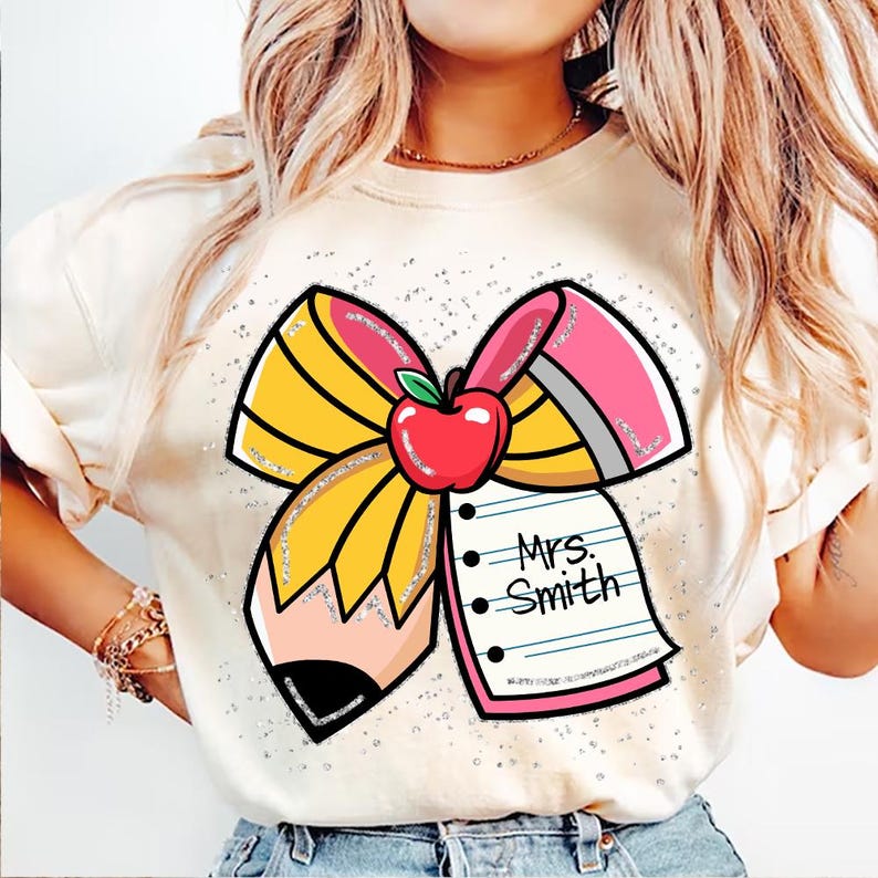 May include: A white t-shirt featuring a pink and yellow pencil bow, a red apple, and a pink notepad with the text "Mrs. Smith" on it.