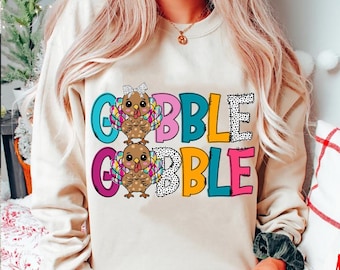 May include: A beige sweatshirt with a colorful graphic of two turkeys and the text "GOBBLE GOBBLE".