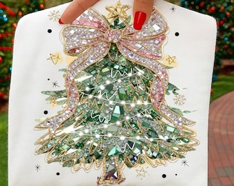 May include: A white Christmas-themed decorative item featuring a sparkling green Christmas tree design adorned with crystals and a pink bow. The tree is embellished with a gold star and string lights. The item is decorated with gold stars and snowflakes.