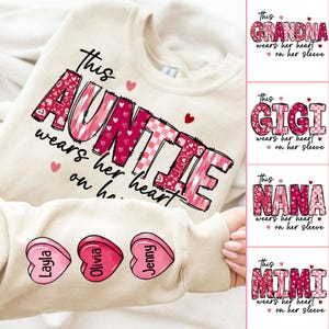 May include: A beige sweatshirt with the text "This Auntie wears her heart on her sleeve" in pink and red patchwork letters. The sweatshirt has three pink candy hearts with the names "Layla", "Olivia", and "Jenny" printed on them.