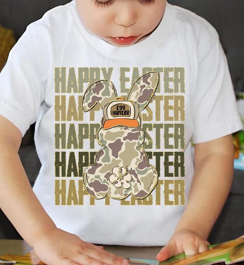May include: White t-shirt with a camouflage Easter bunny wearing a hat that says "Egg Hunter". The words "Happy Easter" are repeated in gold glitter lettering.