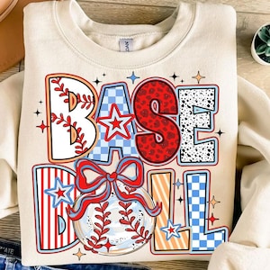 May include: A cream-colored sweatshirt with a colorful graphic design that says "BASEBALL" with a baseball and a bow. The graphic has red, white, blue, and black colors.