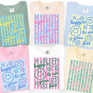 May include: A collection of six t-shirts in various pastel colors, each featuring a smiley face design with the text "happy to see your face." The shirts have a crew neck and short sleeves, perfect for casual wear.
