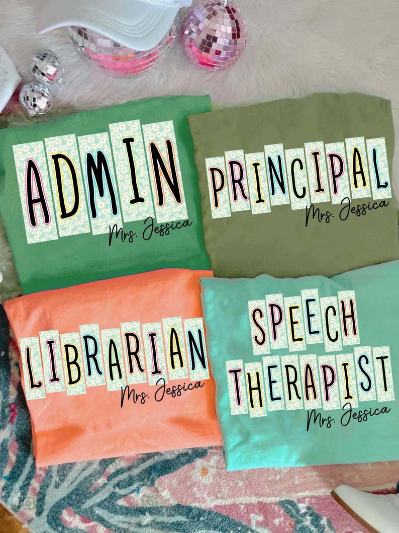 May include: Four brightly coloured t-shirts, each displaying a different job title: "ADMIN", "PRINCIPAL", "LIBRARIAN", and "SPEECH THERAPIST". The shirts are in green, olive green, coral, and teal. Each shirt has the name "Mrs. Jessica" below the title.