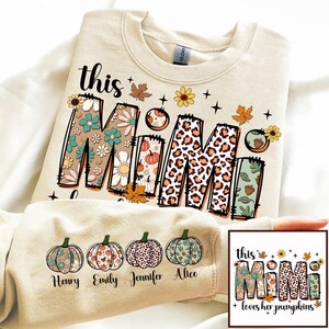 Puede incluir: Una sudadera beige con el texto "this Mimi loves her pumpkins" en un dise&ntilde;o floral y de leopardo. La sudadera tiene cuatro calabazas con los nombres "Henry", "Emily", "Jennifer" y "Alice" impresos debajo.