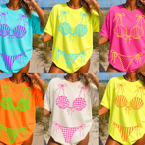 May include: A collection of t-shirts featuring a bikini design. The shirts come in various colors, including light blue, yellow, pink, orange, and cream. Each shirt has a different bikini design, with some featuring seashell or gingham patterns.