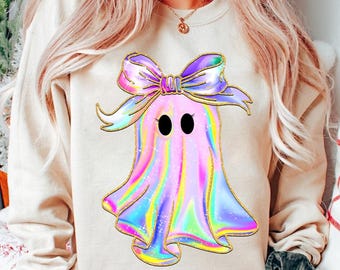Puede incluir: Una sudadera de color crema con un fantasma rosa holográfico que lleva un lazo morado y rosa. El fantasma tiene ojos negros y un diseño brillante iridiscente.