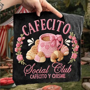 Pode incluir: Almofada preta com bordado rosa "CAFECITO Social Club". O design inclui uma x&iacute;cara de caf&eacute; rosa com la&ccedil;o, croissants e detalhes florais, ideal para um ambiente de caf&eacute;.