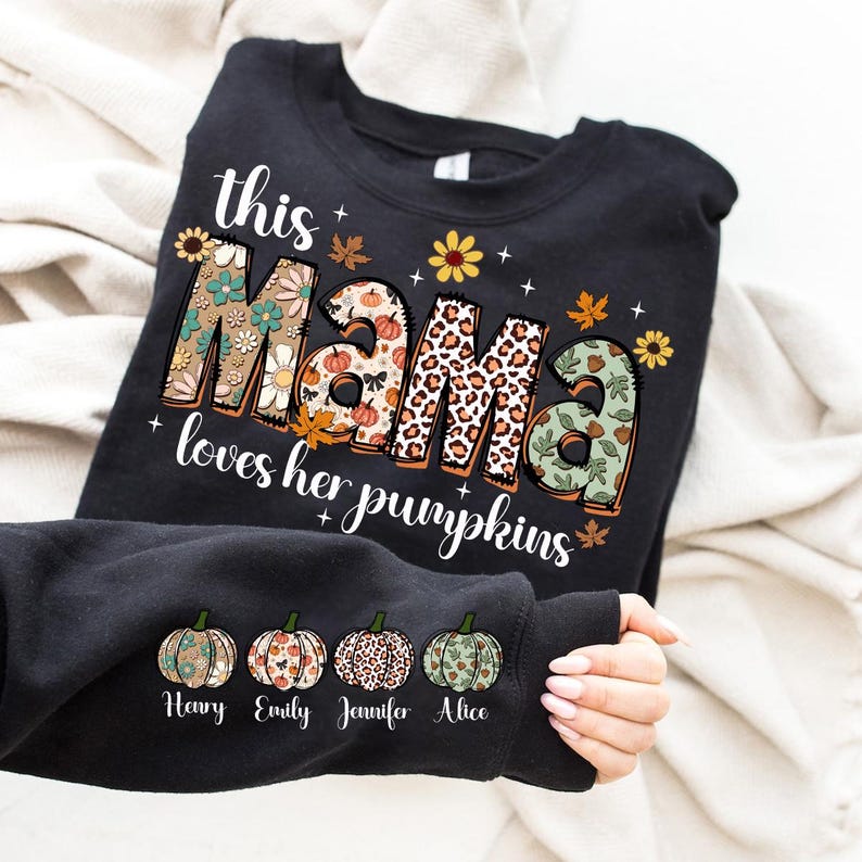 Puede incluir: Sudadera negra con el texto "This Mama loves her pumpkins" en letras de colores con patrones. Cuatro peque&ntilde;as calabazas con los nombres "Henry", "Emily", "Jennifer" y "Alice" est&aacute;n impresas debajo del texto.