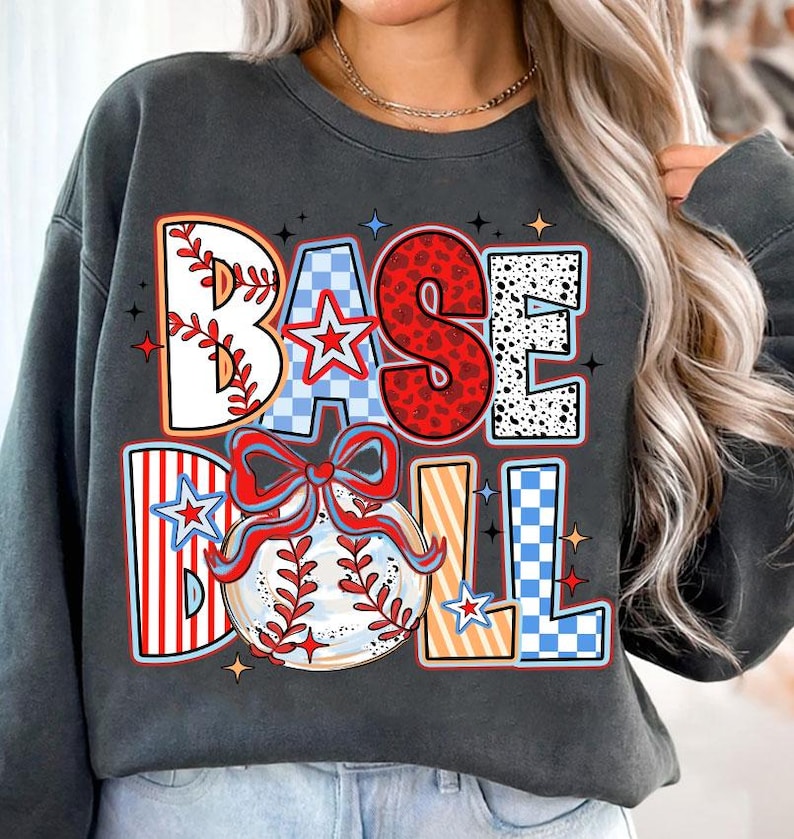 May include: A gray sweatshirt with a colorful graphic design that says "BASEBALL" with a baseball and a bow. The graphic is made up of different patterns like checkered, polka dots, and stripes.