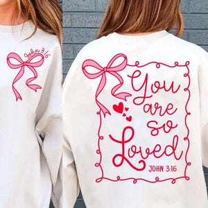 May include: White sweatshirt with a pink bow and the text "You are so Loved" in a red frame with hearts and the text "John 3:16" below.