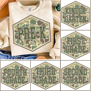 Könnte beinhalten: Ein cremefarbenes Sweatshirt mit einem großen, sechseckigen Grafikdesign mit der Aufschrift "PRE-K" in grünen Buchstaben über einem Tarnmuster. Zusätzliche Grafiken zeigen "Kindergarten", "First Grade", "Fourth Grade", "Third Grade" und "Second Grade".