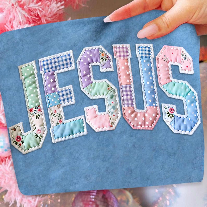 May include: A light blue fabric with the word "JESUS" appliqu&eacute;d in patchwork letters. Each letter is composed of various pastel-colored fabrics, including floral, polka dot, and gingham patterns, outlined with white stitching.