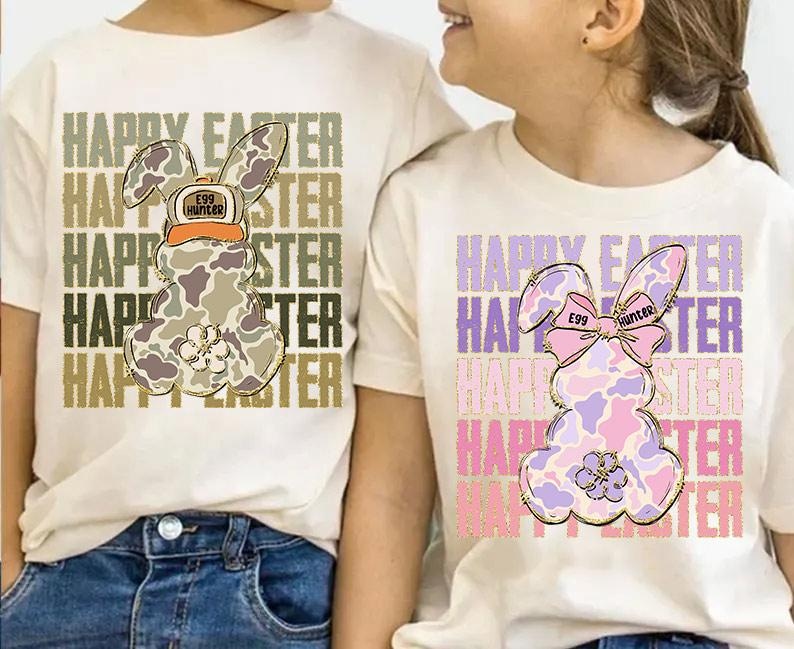 May include: Two white t-shirts with a camouflage bunny rabbit design. The bunny on the left is wearing a hat that says "Egg Hunter". The bunny on the right is wearing a pink bow that says "Egg Hunter". Both shirts have the text "Happy Easter" repeated multiple times.