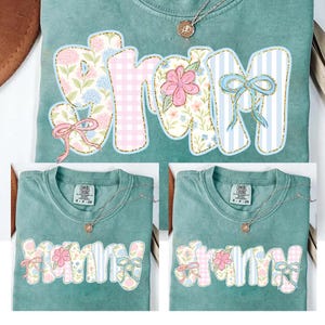 May include: Two green t-shirts with the word "Grammy" printed on them in a patchwork style with floral and gingham patterns. The word is in a light blue, pink, and white color scheme.