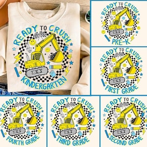May include: A beige sweatshirt with a graphic design of a yellow construction vehicle with the text "Ready to Crush Kindergarten" in a blue and black circle.