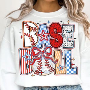 May include: White sweatshirt with a colorful graphic design that says "BASEBALL" with a baseball and a bow. The graphic is made up of different patterns like stripes, polka dots, and checkered.