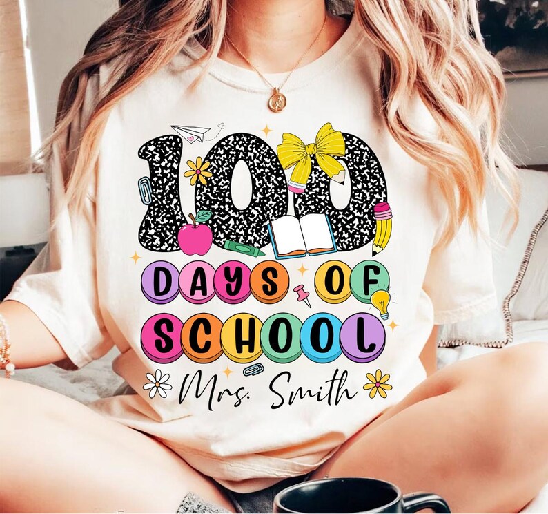 May include: A white t-shirt with a black and white graphic of the number 100 with school supplies. The text "100 Days of School" is in colourful circles. The text "Mrs. Smith" is below the graphic.