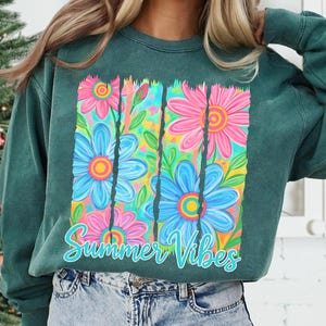 May include: Green sweatshirt with a colorful floral design. The graphic features blue and pink flowers with yellow centers, set against a vibrant background. The words "Summer Vibes" are written in a cursive font.