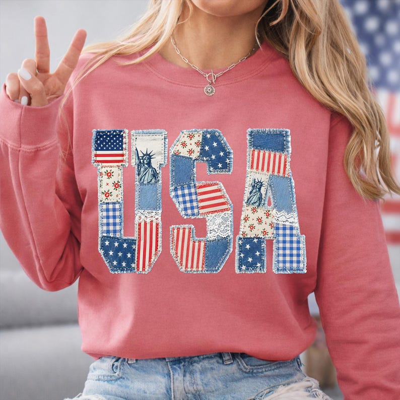 K&ouml;nnte beinhalten: Ein rosafarbenes Sweatshirt mit dem Wort "USA" auf der Vorderseite. Die Buchstaben bestehen aus Patchwork-Denim und Stoff in rot, wei&szlig; und blau, einschlie&szlig;lich Sternen, Streifen und der Freiheitsstatue.