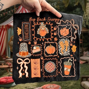 May include: Black Thanksgiving-themed blanket with orange and white illustrations. Features a turkey, pumpkin, pie, and the text "Big Back Energy" and "Thanksgiving". The blanket is held up by a hand.