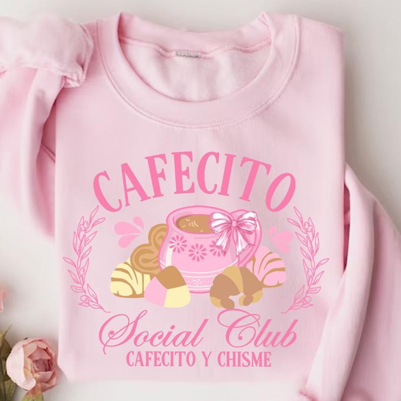 May include: Pink sweatshirt with a graphic design of a coffee cup and pastries. The text reads "Cafecito Social Club Cafecito y Chisme".