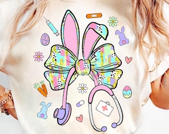 Puede incluir: Camiseta color crema con un diseño colorido con temática de Pascua. El diseño incluye un estetoscopio, orejas de conejo, un lazo y varios gráficos relacionados con la Pascua, como huevos, zanahorias y flores. El diseño es en colores pastel con detalles dorados.