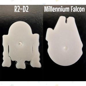 Op de afbeelding: Twee witte 3D-geprinte Star Wars-objecten. E&eacute;n is R2-D2, de andere is de Millennium Falcon. Beide staan op een zwarte achtergrond. De tekst "R2-D2" en "Millennium Falcon" staat boven elk object.