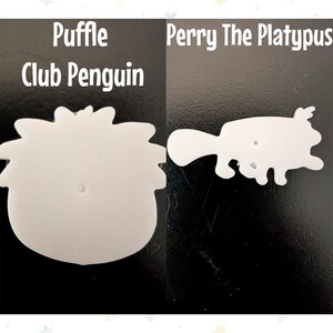 Op de afbeelding: Twee witte uitsparingen van stripfiguren op een zwarte achtergrond. E&eacute;n is een pingu&iuml;n met de tekst "Puffle Club Penguin" erboven. De andere is een vogelbekdier met de tekst "Perry The Platypus" erboven. Beide hebben een gat in het midden.