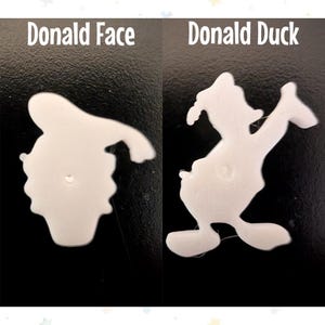 Op de afbeelding: Twee witte plastic uitsparingen van Donald Duck. E&eacute;n is een profiel van Donalds gezicht en de andere is een volledig lichaamsbeeld van Donald Duck. De tekst "Donald Face" en "Donald Duck" staan boven elke uitsparing.