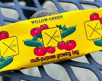 May include: A yellow Willow-Green multi-purpose growing bag featuring illustrations of red tomatoes and green cucumbers. The bag has the text "Willow-Green" and "multi-purpose growing bag" printed on it. The bag is resting on a blue metal surface.